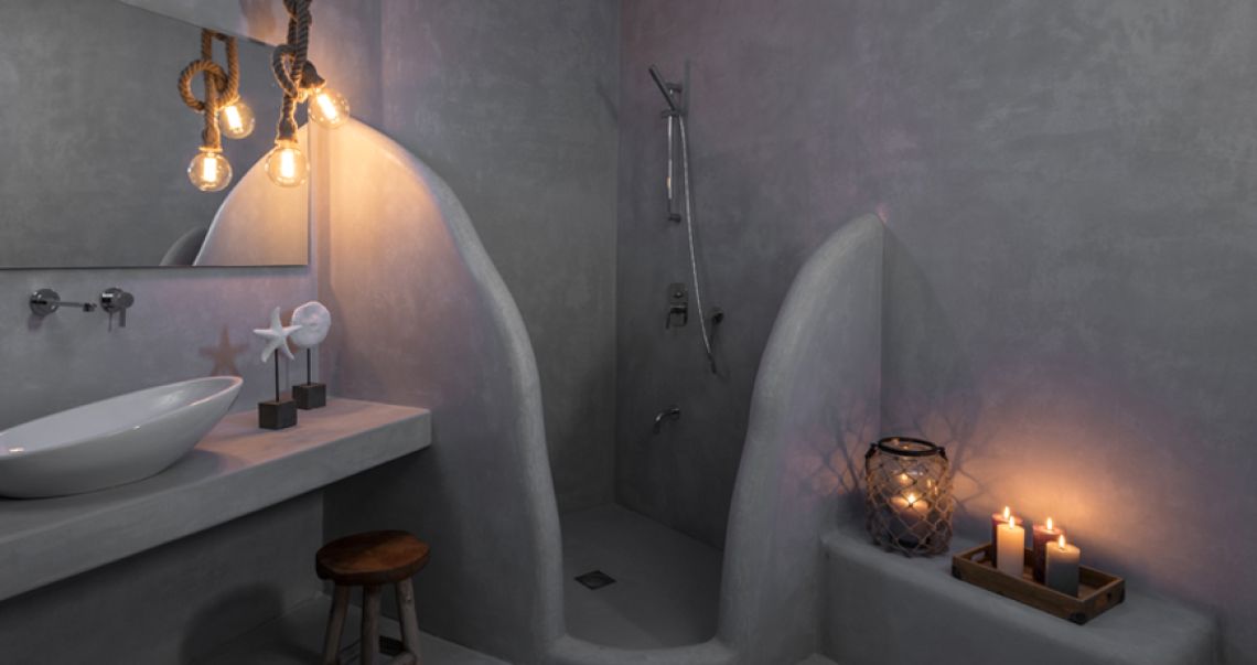 Atmospheric grey microcement bathroom featuring a curved walk-in shower, a floating vanity with a vessel sink, and rustic rope pendant lighting.