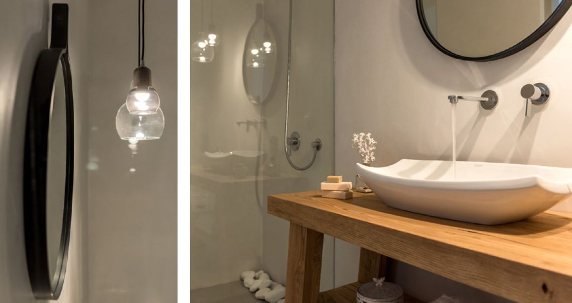 Split view of a modern bathroom featuring a round black mirror and glass pendant lights on the left, and a vessel sink on a wooden vanity on the right.