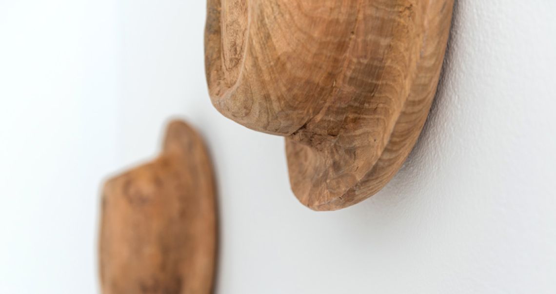 Close-up detail of rustic, hand-carved wooden wall art pieces mounted on a smooth white wall.
