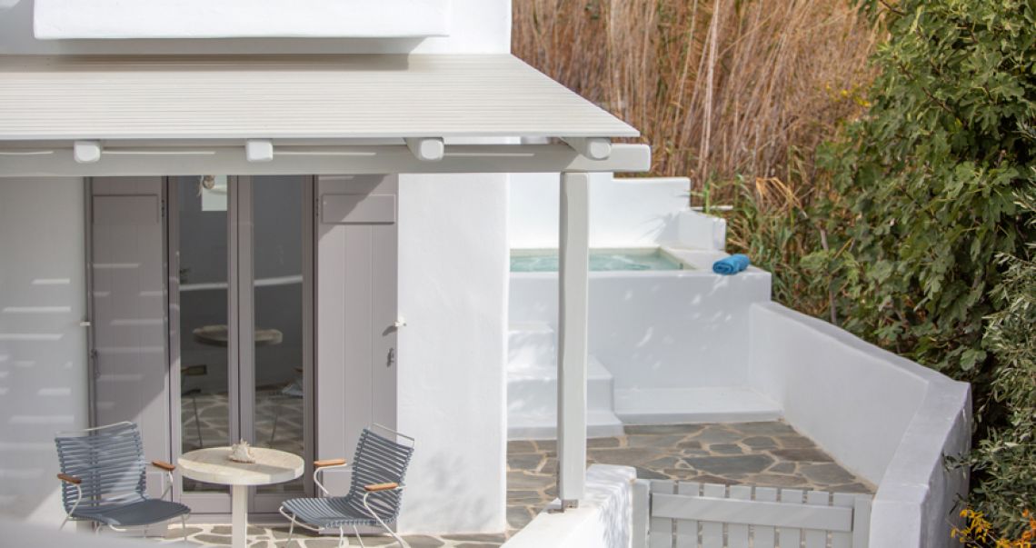 Private white terrace featuring a small outdoor plunge pool, grey lounge chairs, and a small table, framed by lush greenery.